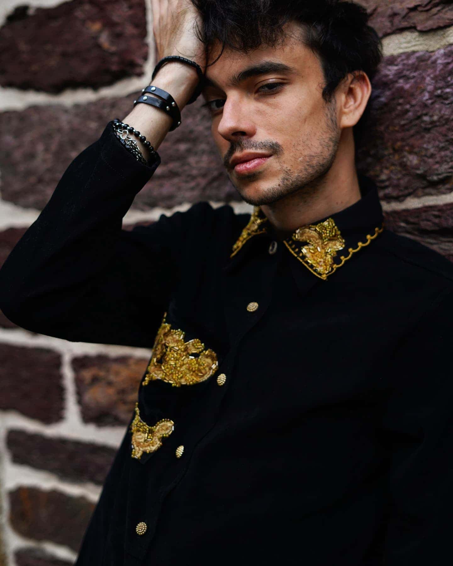 Chemise noire portée, col et poitrine brodés de motifs dorés, boutons dorés