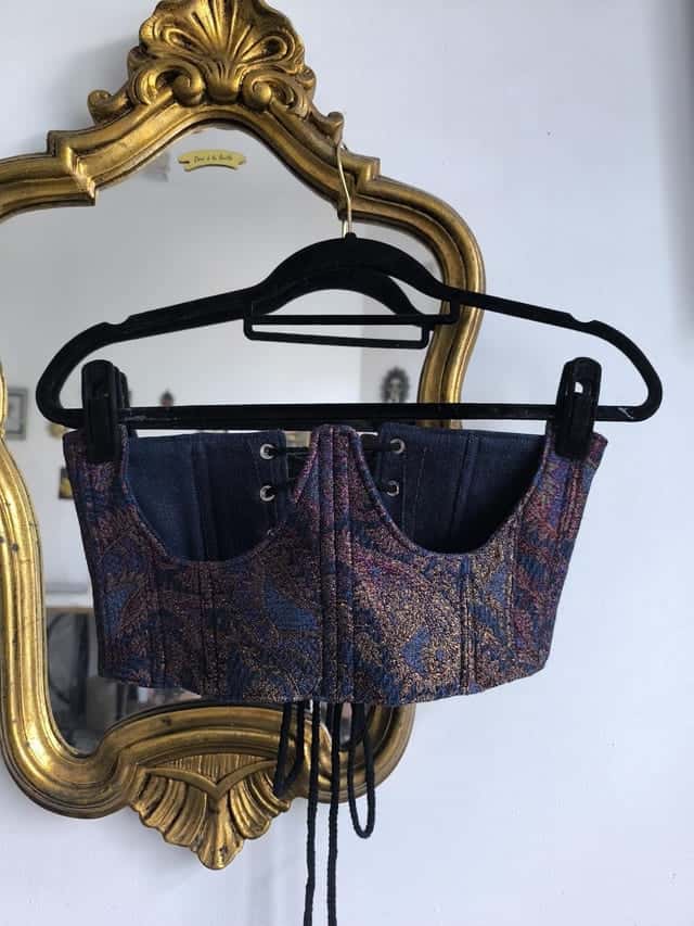 Corset à motif cachemire sur un cintre devant un miroir doré, empiècements en jean