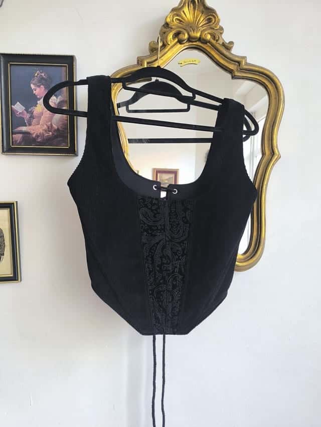 Corset noir en velours côtelé sur un cintre devant un miroir doré