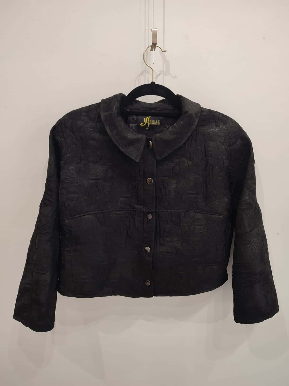 Veste noire courte à motifs en relief sur un cintre, petit col et boutons pression