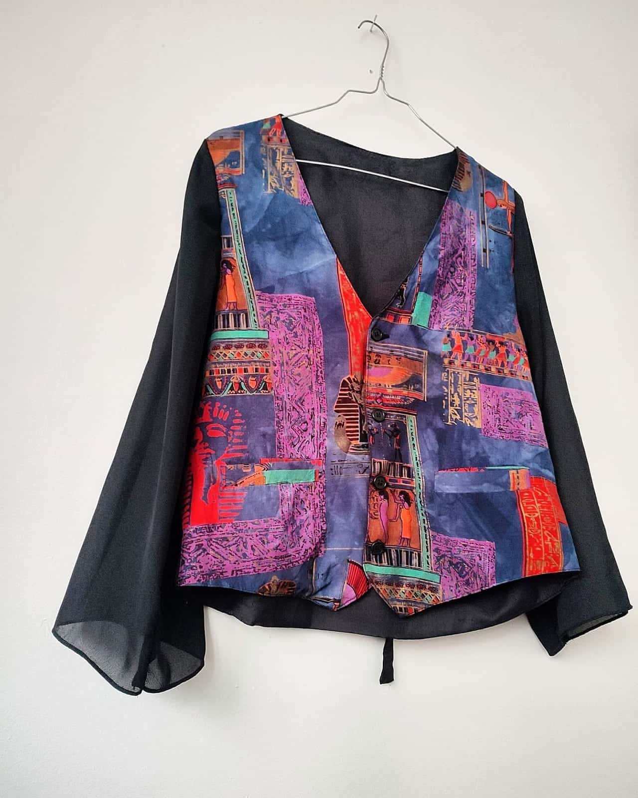 Gilet en patchwork imprimé sur une chemise noire transparente à manches évasées, sur un cintre