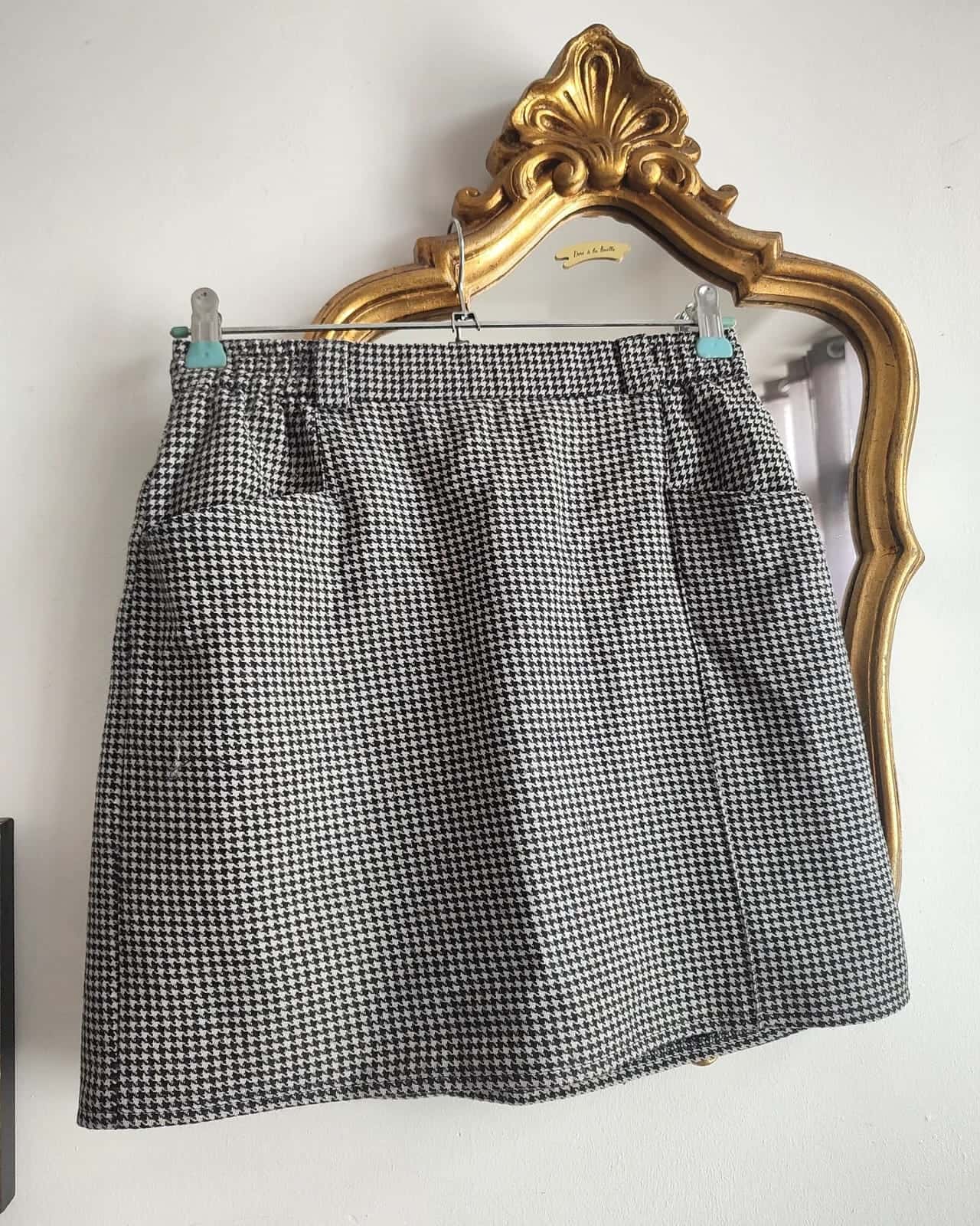 Jupe courte pied-de-poule noir et blanc sur un cintre, devant un miroir doré