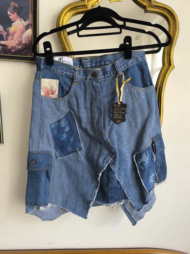 Jupe en jean sur un cintre, ourlet en pointes coupé à vif, poches cargo et empiècements au cyanotype