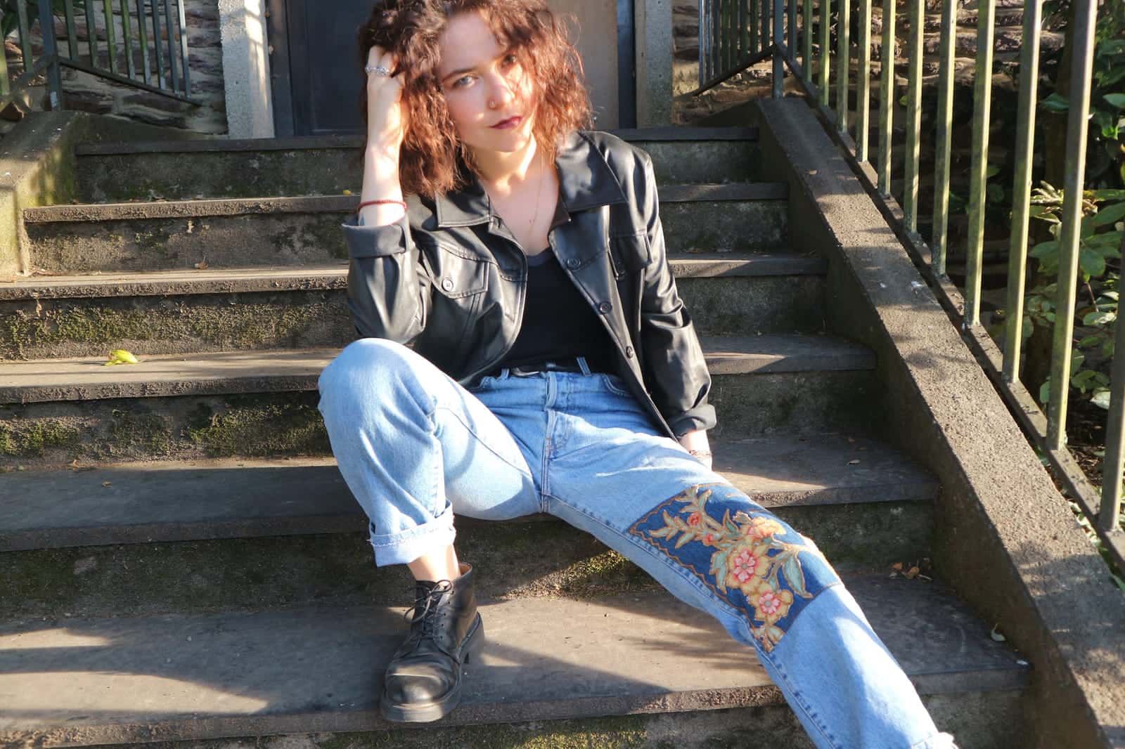 Veste de cuir noire portée avec un jean clair, un empiècement fleuri sur le bas d’une jambe