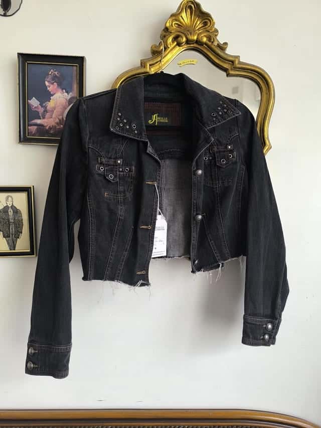 Veste en jean noir courte sur un cintre, col et épaules cloutés