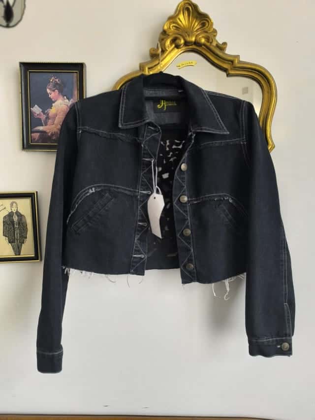 Veste en jean noir courte sur un cintre, vue de face
