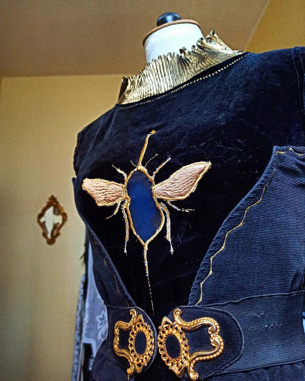 Haut de velours bleu nuit sur un mannequin de couture, brodé d’une abeille aux ailes dorées, deux fermoirs dorés à la taille